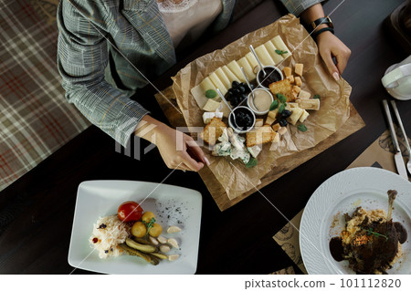 Young woman sitting at a table in the restaurant and eating set of cheese. Tasty snack. Beautiful serving of food in the cafe. Top view. Lifestyle Young woman sitting at a table in the restaurant and eating set of cheese. Tasty snack. Beautiful serving of food in the cafe. Top view. Lifestyle 101112820