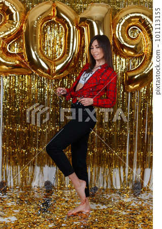 Beautiful happy woman in stylish clothes posing at a party against the background of golden balloons 2019. Girl is having fun and enjoying the holiday. The concept of celebrating Christmas 101113155