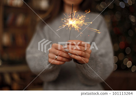 Woman in knitted sweater celebrates the holiday with amazing sparklers in female hands. Close-up. Woman in knitted sweater celebrates the holiday with amazing sparklers in female hands. Close-up. 101113264