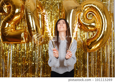Happy joyful young woman happily holds in her hands fireworks on the background of balloons 2019 in the festive room. Cute girl celebrates the New Year. Magical celebration atmosphere. Happy joyful young woman happily holds in her hands fireworks on the background of balloons 2019 in the festive room. Cute girl celebrates the New Year. Magical celebration atmosphere. 101113269