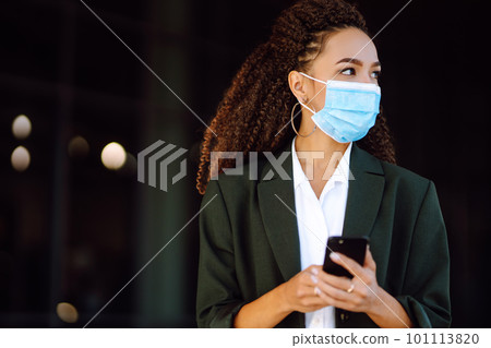 Portrait of a business woman wearing a protective mask with phone solves work issues. Covid-2019. 101113820