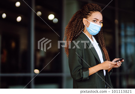 Portrait of a business woman wearing a protective mask with phone solves work issues. Covid-2019. 101113821