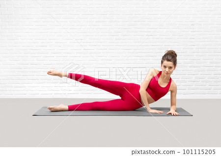 Attractive young woman lying on a side and does leg kicks exercise indoor in loft studio. Attractive young woman lying on a side and does leg kicks exercise indoor in loft studio. 101115205