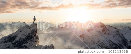 Adventurous Man Hiker standing on top of icy peak with rocky mountains in background. 101115916