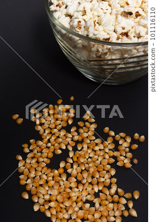 Ready-to-eat popcorn in a glass bowl and corn kernels on a black background. 101116110