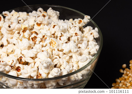 A bowl of fried popcorn and corn kernels on a black background 101116111