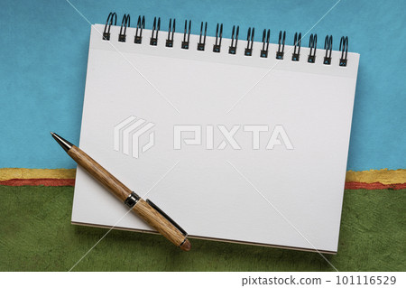 blank spiral sketchbook with white pages with a pen against colorful abstract landscape 101116529