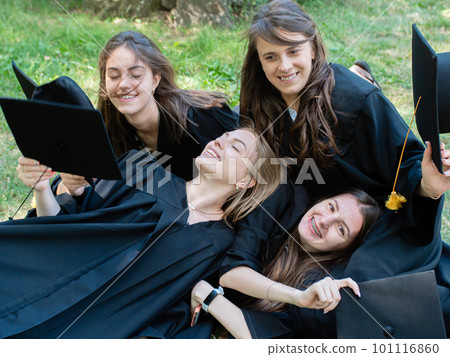 Several young smiling female students in black graduation gowns lie on the grass in the university park Several young smiling female students in black graduation gowns lie on the grass in the university park 101116860