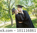 Graduates in robes stand in a university whipping and kiss 101116861