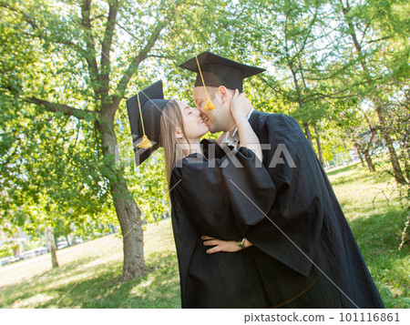 Graduates in robes stand in a university whipping and kiss Graduates in robes stand in a university whipping and kiss 101116861