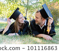 Happy guy and girl look at each other lying on the lawn in a black graduate gown and an academic cap of the university 101116863