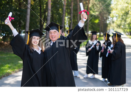 A group of graduates in robes outdoors. An elderly man and a young woman congratulate each other on their graduation. A group of graduates in robes outdoors. An elderly man and a young woman congratulate each other on their graduation. 101117729