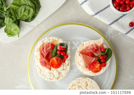 Puffed rice cakes with prosciutto, berries and basil on grey marble table, flat lay 101117899