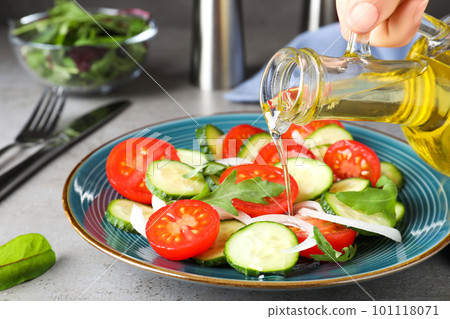 Woman adding cooking oil to delicious salad on grey table, closeup Woman adding cooking oil to delicious salad on grey table, closeup 101118071