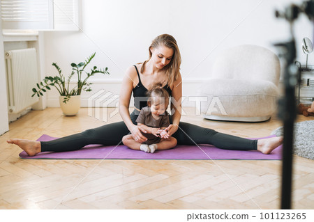 Young woman with little daughter doing exercises and recording video on mobile phone in studio Young woman with little daughter doing exercises and recording video on mobile phone in studio 101123265
