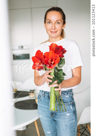 Young woman with bouquet of red flowers in hands near window in bright kitchen at home 101123413