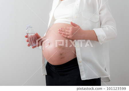 Pregnant woman applying cosmetic oil on her belly for healing puncture marks, bruises and stretches 101123599