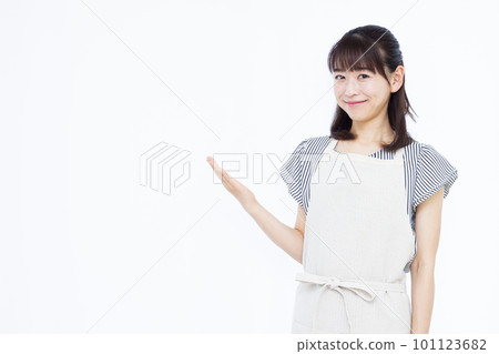 A housewife in her thirties in an apron who is guiding in front of a white background 101123682