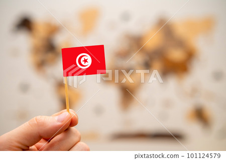 Tunisia flag in mans hand on the wooden world map background. Global economy and geopolitics concept.  101124579