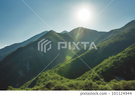 Beautiful sunrise over the green mountains in morning light with fluffy clouds on a bright blue sky. Nature freshness concept 101124944
