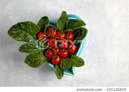 Green spinach leaves and red cherry tomatoes on a heart shaped blue plate on a light concrete table Green spinach leaves and red cherry tomatoes on a heart shaped blue plate on a light concrete table 101126859