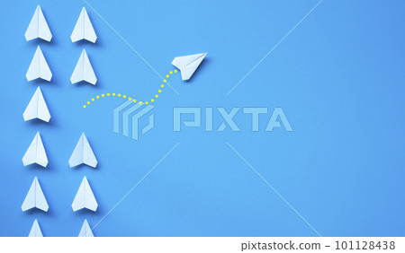 Top view of white paper airplane origami leaving other white airplanes on blue background with customizable space for text or ideas. Leadership skills concept and copy space. 101128438