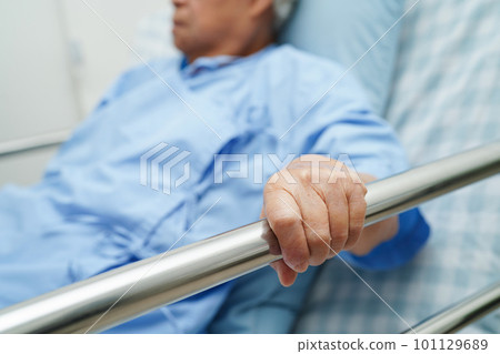 Asian elder senior woman patient holding bed rail while lie down with hope waiting her family in hospital. 101129689