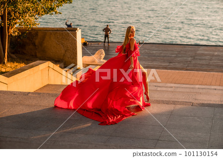 Sunrise red dress. A woman in a long red dress against the backdrop of sunrise, bright golden light of the sun's rays. The concept of femininity, harmony. 101130154