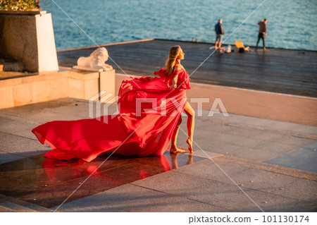 Sunrise red dress. A woman in a long red dress against the backdrop of sunrise, bright golden light of the sun's rays. The concept of femininity, harmony. 101130174
