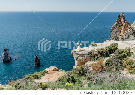Woman in a yellow dress on the sea. Side view Young beautiful sensual woman in yellow long dress posing on a rock high above the sea at sunset. Girl in nature against the blue sky Woman in a yellow dress on the sea. Side view Young beautiful sensual woman in yellow long dress posing on a rock high above the sea at sunset. Girl in nature against the blue sky 101130189