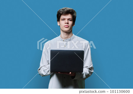 Portrait of young college student guy using laptop on blue background Portrait of young college student guy using laptop on blue background 101130600
