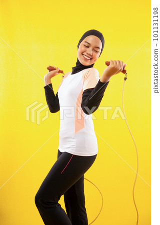 smiling Asian Muslim woman exercising skipping rope on a yellow smiling Asian Muslim woman exercising skipping rope on a yellow 101131198