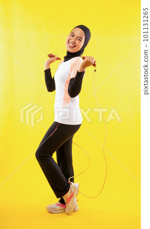 Side view of Muslim woman exercising skipping rope on yellow Side view of Muslim woman exercising skipping rope on yellow 101131265