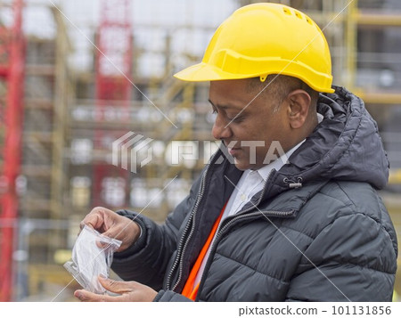 Indian construction worker taking out his ffp2 protective mask before his work shift Indian construction worker taking out his ffp2 protective mask before his work shift 101131856