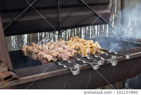 Shish kebab from different types of meat on skewers is fried on fire and coals in the grill 101133960
