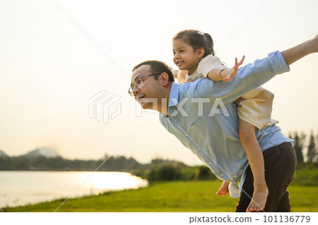 Happy father holding daughter on back playing together in garden 101136779