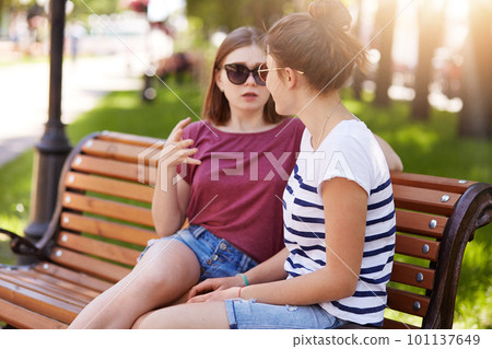 Young cute girl tells her loyal beautiful friend scary old story. Cheerful girl makes her friend believe in fictional story and wants to scare poor creature to death. Friend relations concept. 101137649