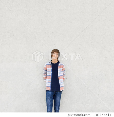 Young boy with trendy haircut wearing shirt and jeans standing near white concrete wall having serious expression. Stylish teenger posing into camera while being isolated over white background Young boy with trendy haircut wearing shirt and jeans standing near white concrete wall having serious expression. Stylish teenger posing into camera while being isolated over white background 101138315