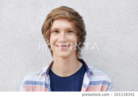 Handsome stylish schoolboy with trendy hairstyle wearing shirt looking with smile into camera having dark narrow eyes and thin lips. Fashionable young hipster guy having appealing appearance 101138342
