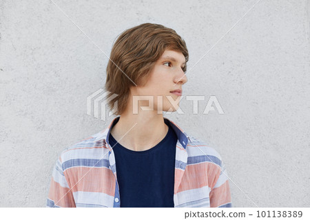 Portrait of teenage boy with trendy hairstyle wearing T-shirt and shirt looking away having deep thoughts while standing over white concrete wall. Serious hipster guy isolated over white background Portrait of teenage boy with trendy hairstyle wearing T-shirt and shirt looking away having deep thoughts while standing over white concrete wall. Serious hipster guy isolated over white background 101138389