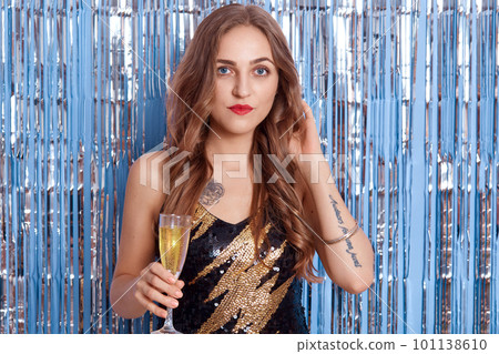 Portrait of beautiful young woman in beautiful cocktail black dress, girl holding glass with wine or champagne in her hands, posing against white background. 101138610