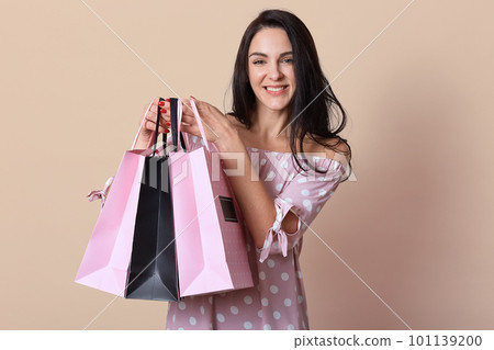 Indoor studio shot of positive energetic young cute female holding bags with purchases in both hands, being in high spirits, spending free time in shopping mall. People and shopping concept. 101139200