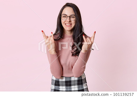 Portrait of sincere cheerful brunette young model having happy facial expression, smiling, making gestures, showing rock signs. Copy space for advertisement. People, beauty and emotions concept. Portrait of sincere cheerful brunette young model having happy facial expression, smiling, making gestures, showing rock signs. Copy space for advertisement. People, beauty and emotions concept. 101139257