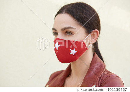 Closeup portrait of brunette woman wearing brown leather jacket and stylish red protective mask with white stars, beautiful lady looking at distance, female has clean skin, looks thoughtful. Closeup portrait of brunette woman wearing brown leather jacket and stylish red protective mask with white stars, beautiful lady looking at distance, female has clean skin, looks thoughtful. 101139567