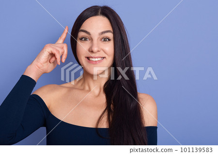 Photo of nice smiling lady wearing dress posing isolated over blue background pointing her finger in eureka sign, having great innovative idea, having solution of problem. Photo of nice smiling lady wearing dress posing isolated over blue background pointing her finger in eureka sign, having great innovative idea, having solution of problem. 101139583