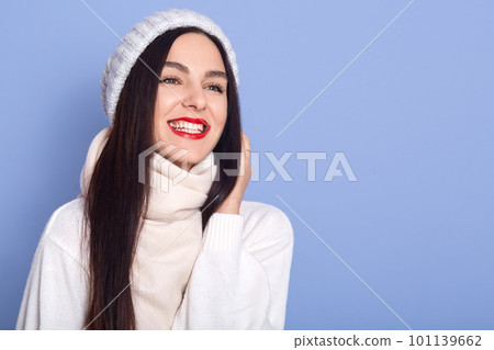 Close up portrait of beautiful winter woman in warm clothing, lady looking aside with charming smile, dresses white sweater, posing with red lips. Copy space foe advertiment or promotional text. 101139662