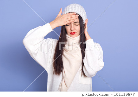 Horizontal indoor picture of exhausted ill sweet young lady closing eyes, putting hand on forehead, having fever, putting hand on ear, having earache, feeling bad. People and health concept. 101139677