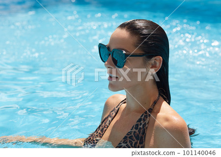 Profile view of beautiful stunning elegant brunette model woman with perfect face in swim suit with leopard print and sunglasses standing in pool, sensually looks into distance. Luxury resort concept. 101140046