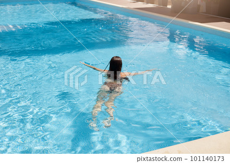 Outdoor picture of dark haired woman back view, relaxing in swimming pool, swimming professionally, having luxury rest, enjoying time at hotel spa resort, improving her swimming skills. Rest concept. Outdoor picture of dark haired woman back view, relaxing in swimming pool, swimming professionally, having luxury rest, enjoying time at hotel spa resort, improving her swimming skills. Rest concept. 101140173