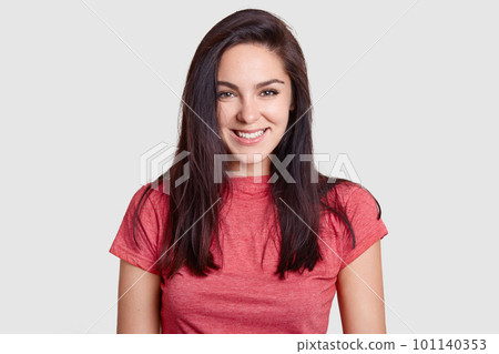 Beautiful brunette woman with pleasant smile, dark hair, dressed in casual pink t shirt, has white perfect teeth, rejoices recieving compliment, isolated on white background. Positive emotions concept Beautiful brunette woman with pleasant smile, dark hair, dressed in casual pink t shirt, has white perfect teeth, rejoices recieving compliment, isolated on white background. Positive emotions concept 101140353